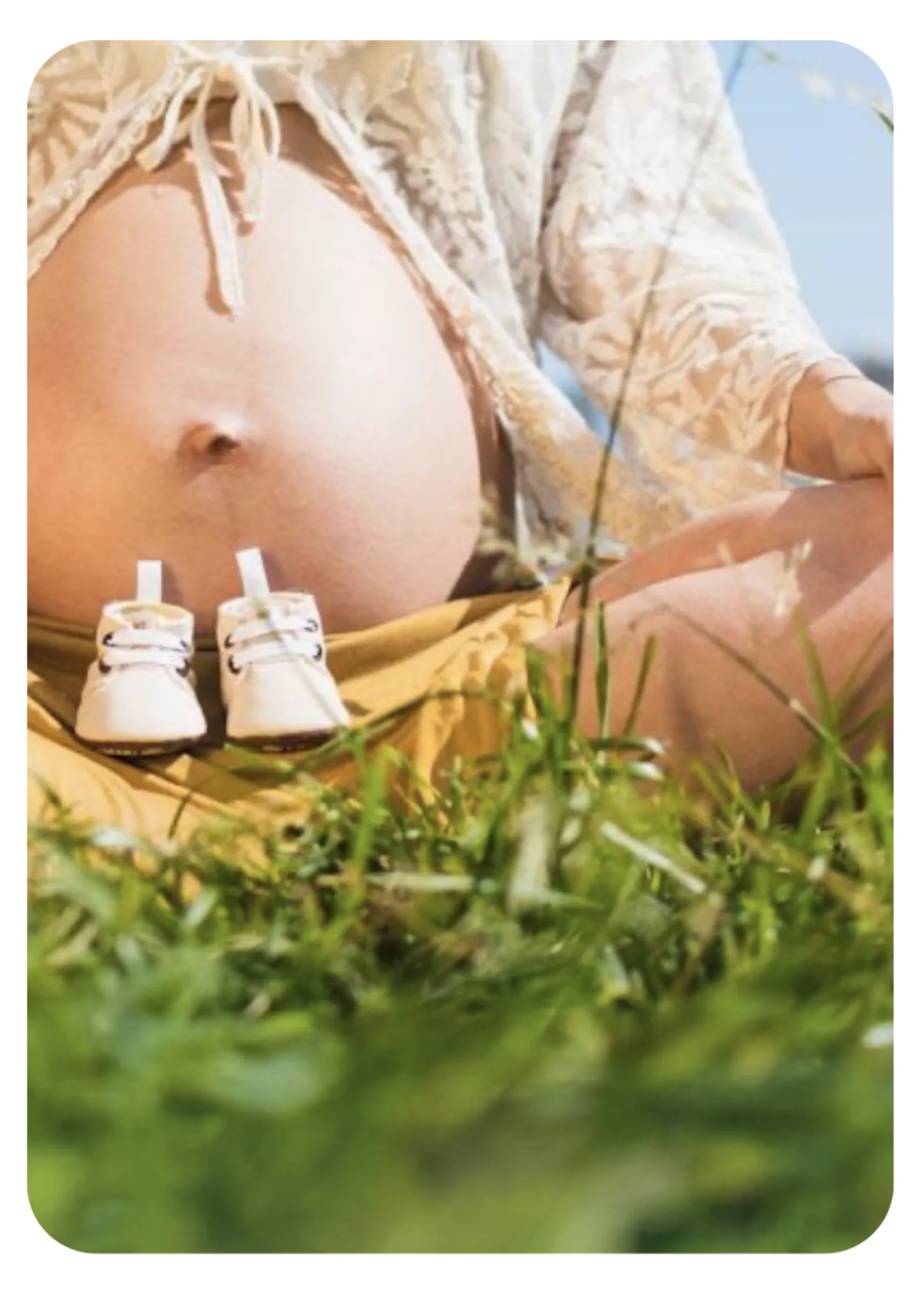 Pregnant woman resting outdoors with tiny baby shoes on her belly