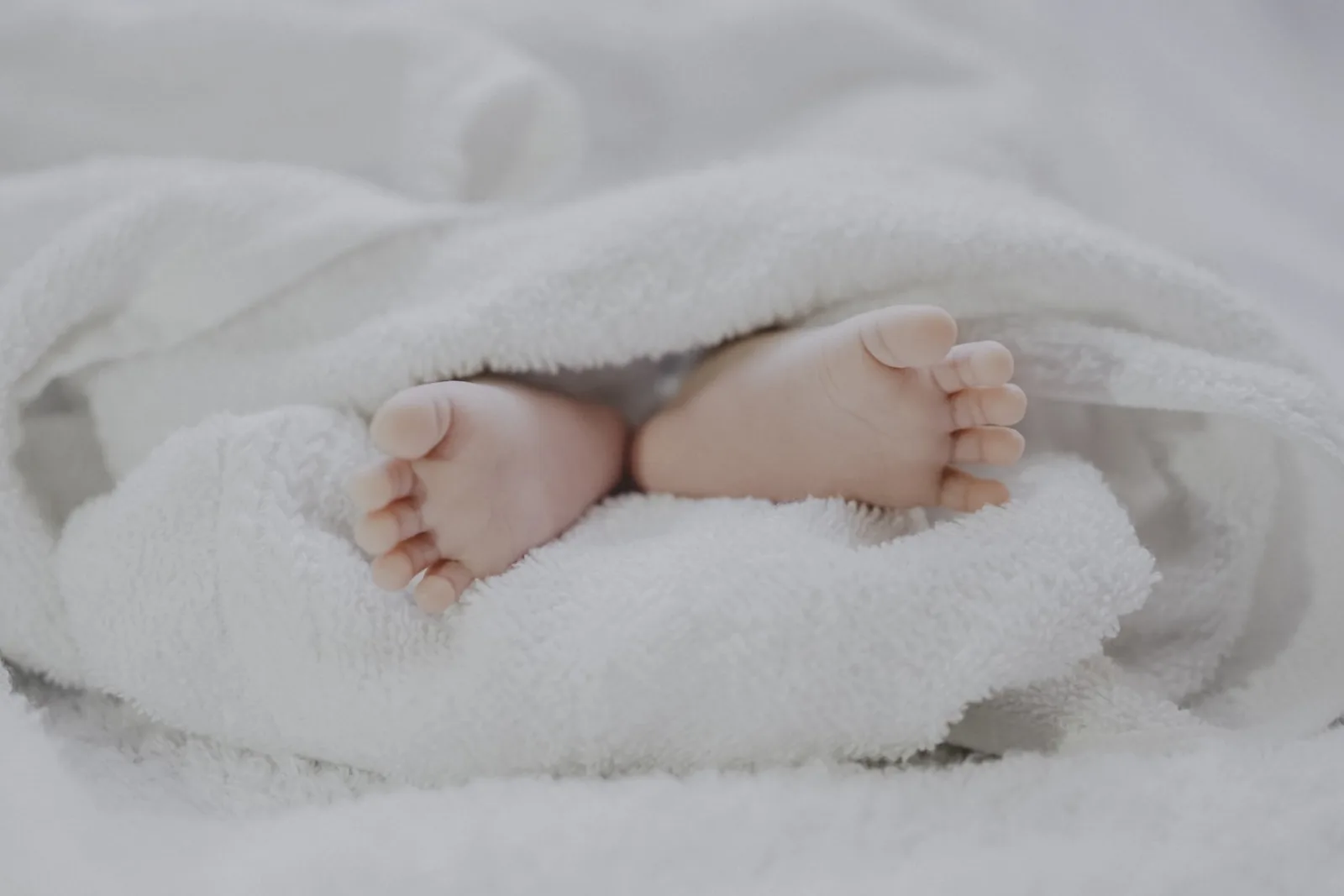 Newborn baby feet peeking out from a soft white blanket