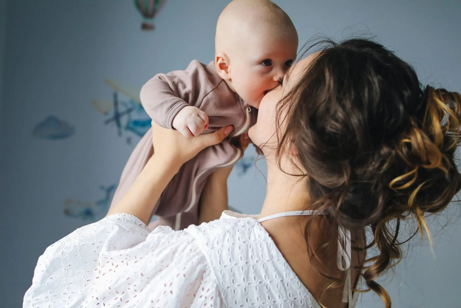 Mother lifting and kissing her baby in a softly lit nursery